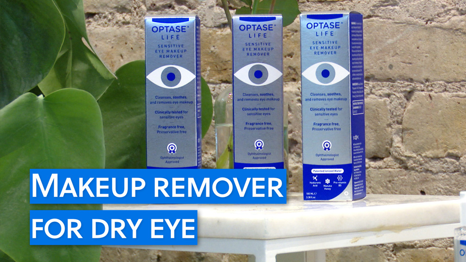 Three silver and blue boxes with an illustration of a simple eye and branding reading ‘Optase Life Sensitive Eye Makeup Remover’ stand on a white marble table surrounded by lush green leaves