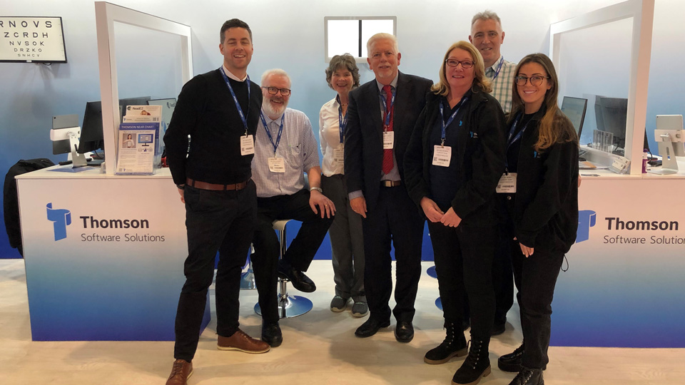 The Thomson Software Solutions team stands smiling on an exhibition stand with the company’s branding