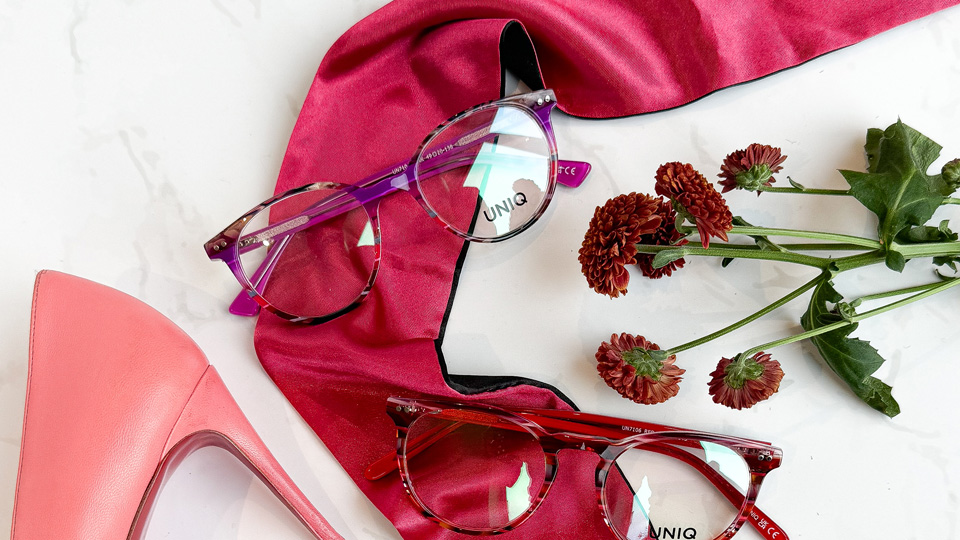 Three frames in patterns ranging from red to pink are arranged over a pink silk ribbon laid out on a marble backdrop. The spiked heel of a pink shoe is arranged on one side, and red flowers are laid on the other 
