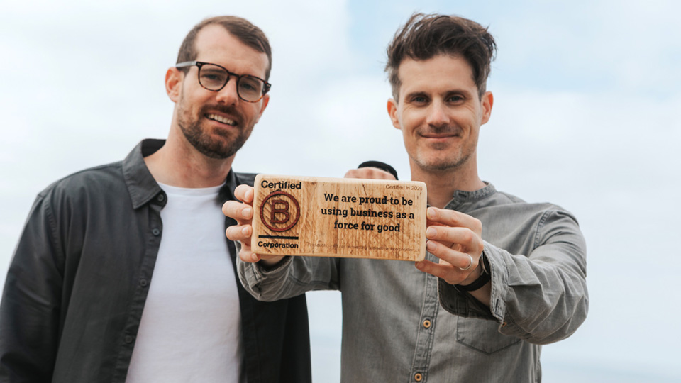 The founders of Bird Eyewear hold up a small wooden plaque that celebrates the certification of the brand as a B Corp 