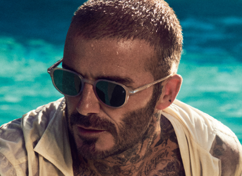 David Beckham wears a pair of sandy colours sunglasses from his collection in a summery pool-side image