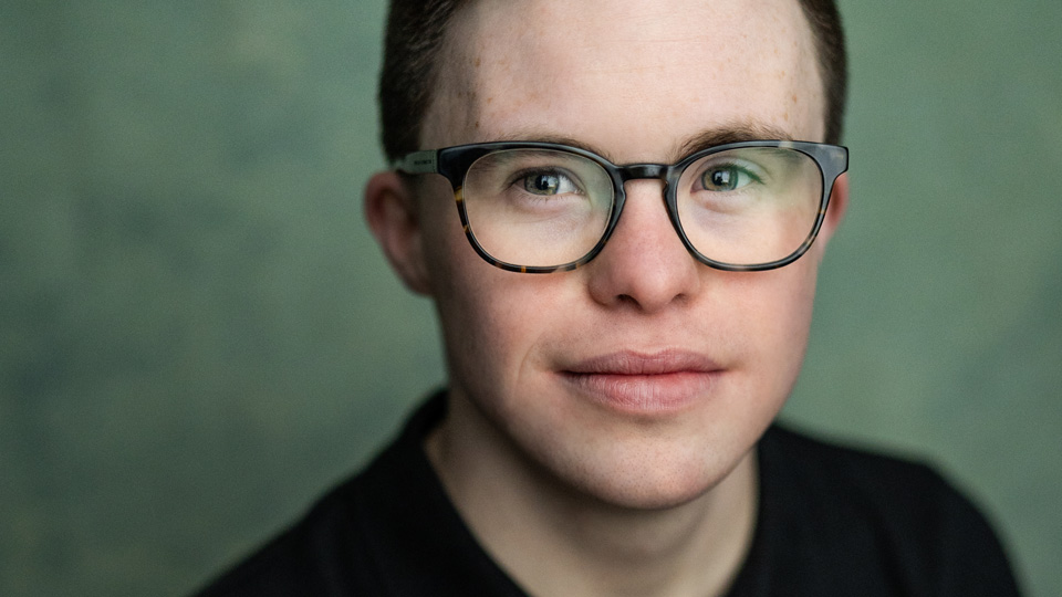 George wears square glasses with a dark tortoiseshell style frame