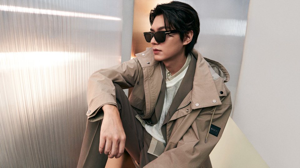Lee Minho wears dark sunglasses and a tan trench coat 