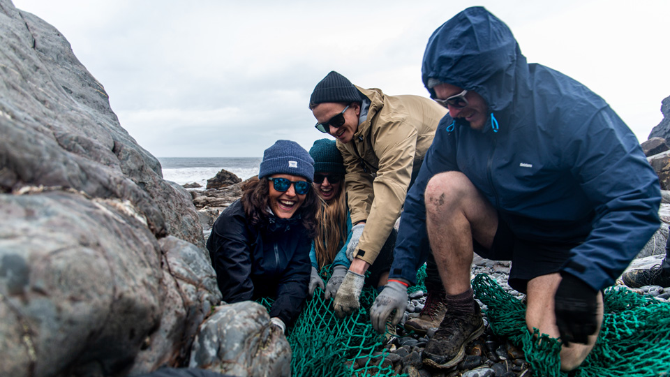 A group of people are untangling a discarded fishing net from boulders on a Cornish beach