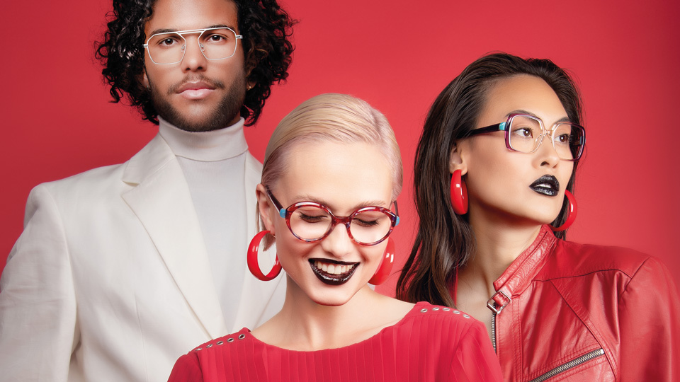 Three people stand in front of a red background wearing a mixture of red white and black