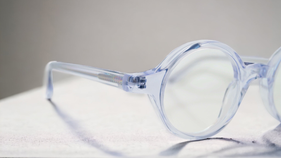 A clear acetate frame is angled so only the left lens and arm are displayed. The side of the frame is slightly broader, to provide coverage for a thicker lens.