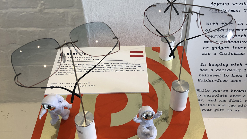Clipped to displays on a red and gold box are three frames from the latest Titan Minimal Art collection. Each of the models is oversized and square-d, but with a quirky shape to the bottom edge of the light blue lens. Two little figurines of astronauts are arranged playfully around the frames