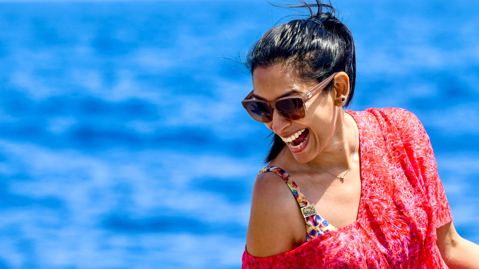 Sima Sthanakiya poses on the beach, smiling down at the waves through sunglasses