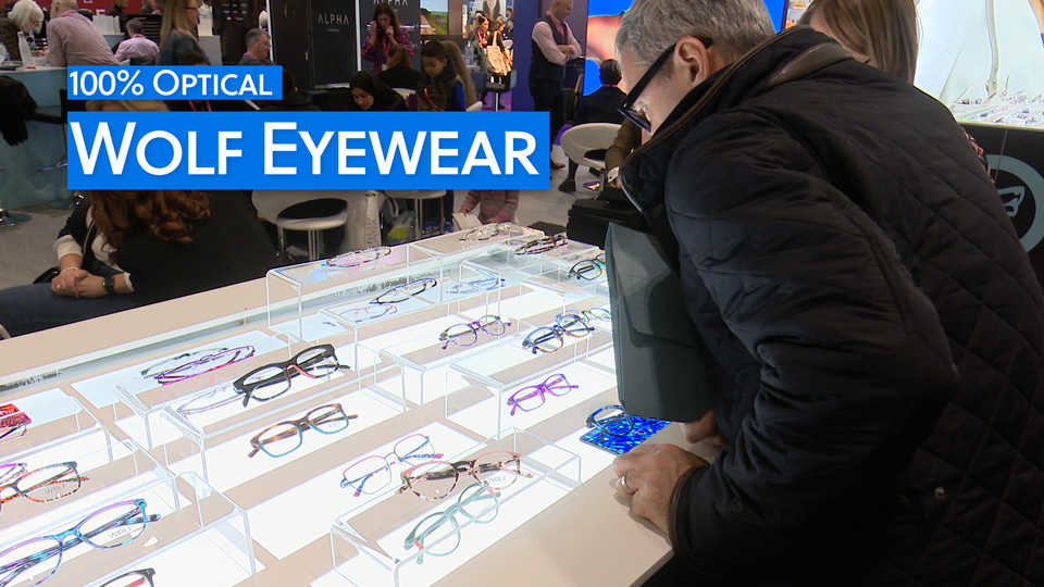  A man leans over a lit display of Wolf Eyewear frames, the colours bright against the box light 