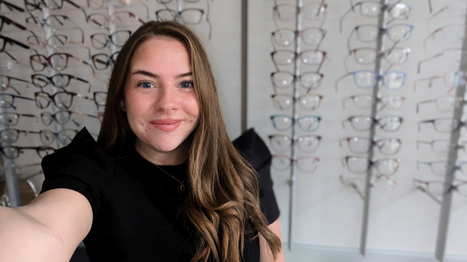 Suzanne smiles for the camera against a backdrop of a glasses display in practice