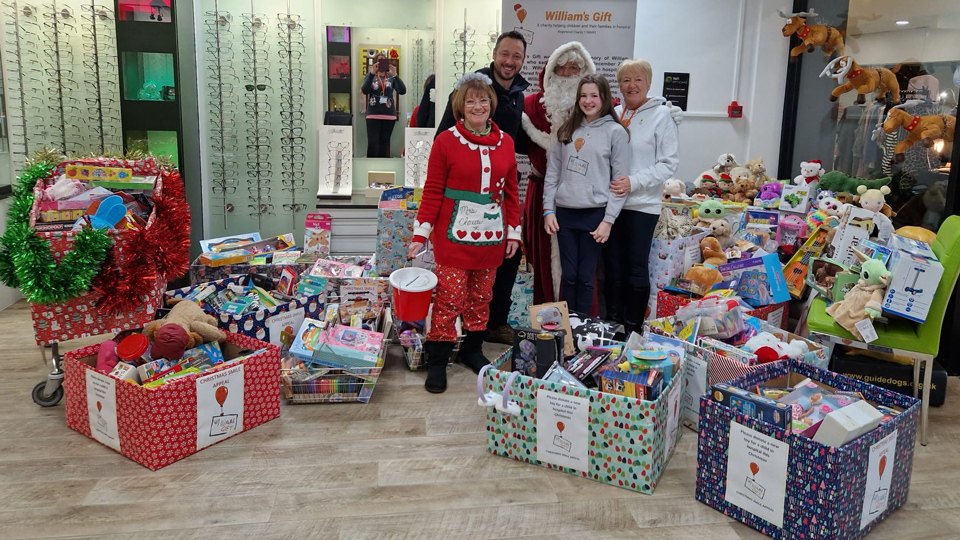 Practice team members, representatives of William’s Gift, and a Father Christmas stand in the Valli practice surrounded by toy donations