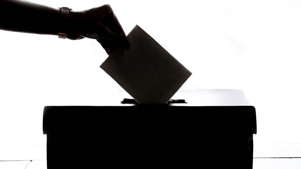 A silhouette of a hand dropping a card into a ballot box