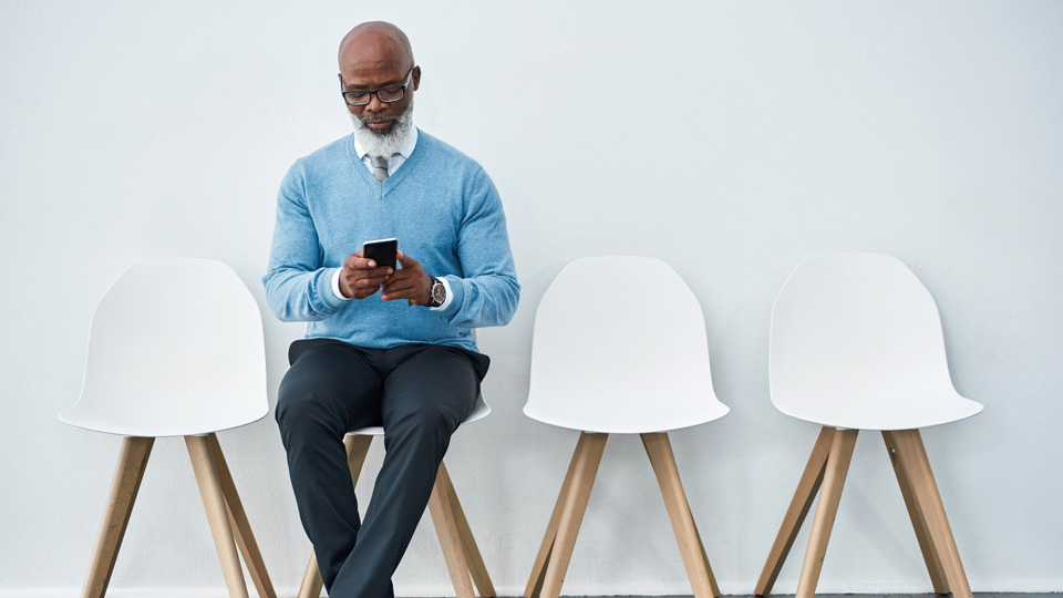Studio shot of a mature businessman wearing glasses and using a mobile phone while waiting for an appointment
