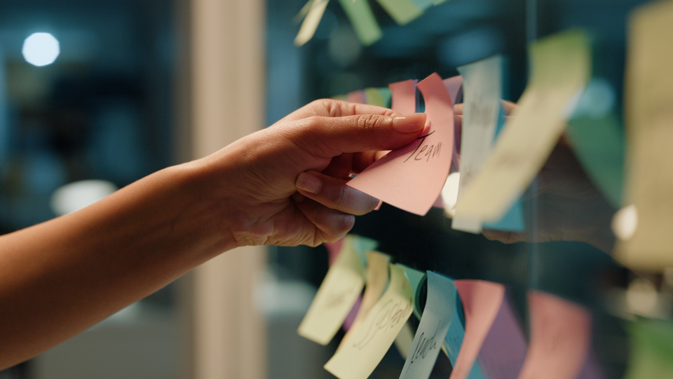 A hand places sticky notes onto a glass office wall