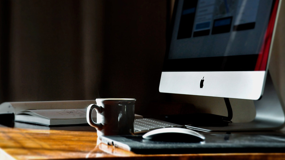 A desk with MacBook screen, open books and coffee cup