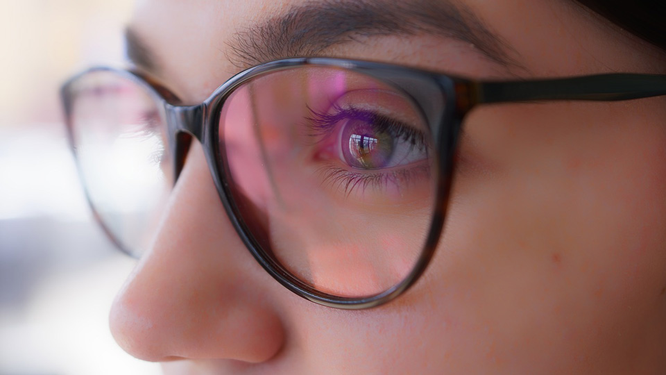A close up of a woman with dark hair and green eyes wearing a pair of spectacles with black frames
