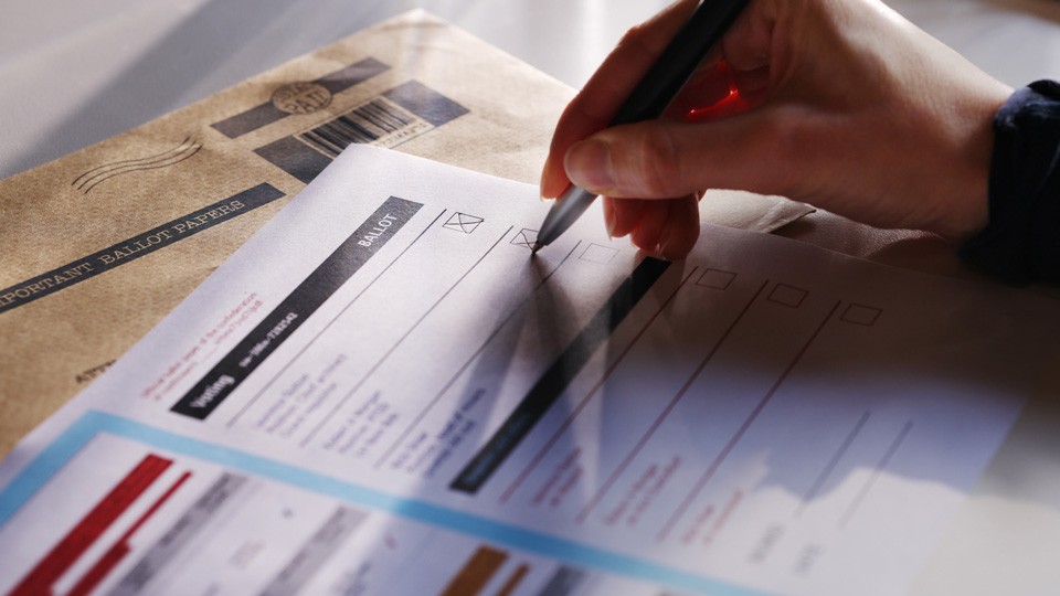 A close up of a hand completing an election ballot paper 