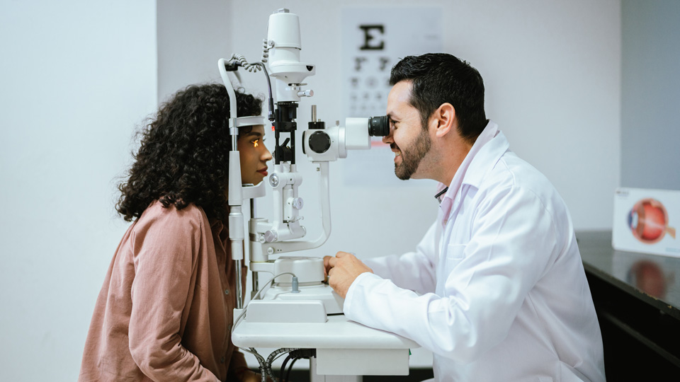 A young woman is positioned at a slit lamp while the optometrist conducts an eye exam