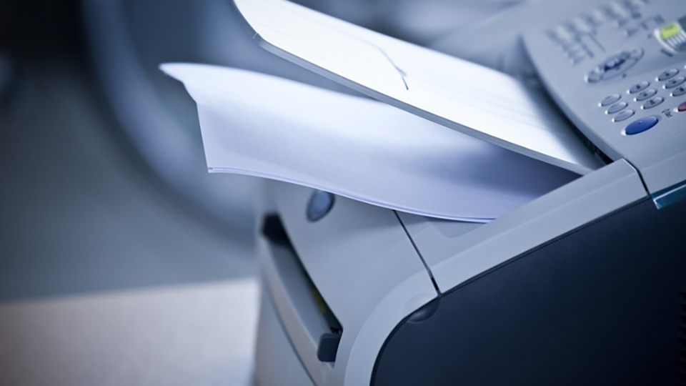 A printer is shown in profile with pages of blank paper in the printing tray