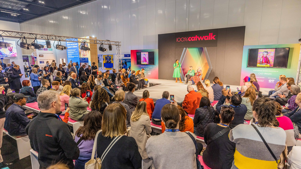 An audience are watching a panel discussion on the Catwalk at 100% Optical