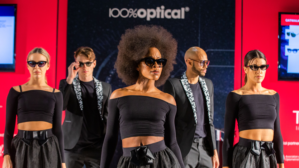 Five models all dressed in black wearing sunglasses on the catwalk at 100% Optical. 
