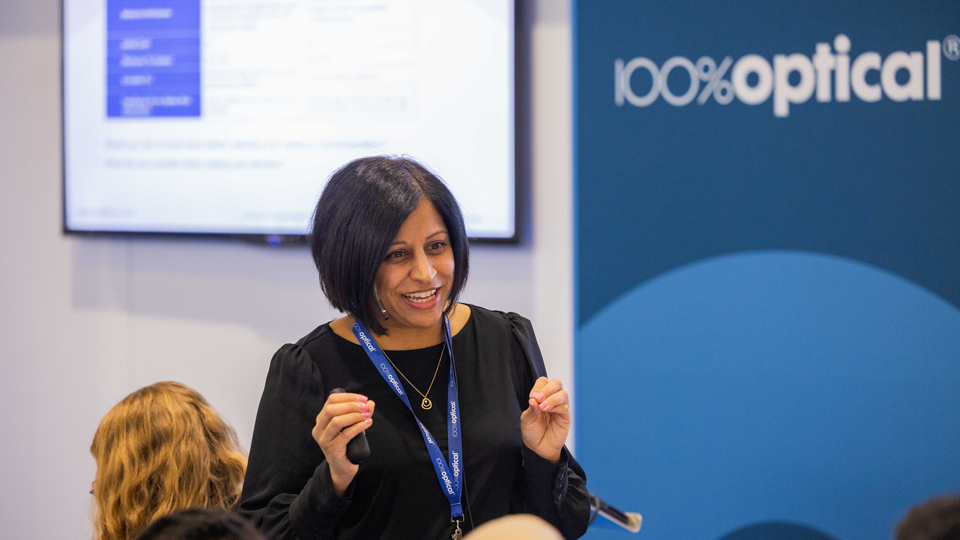 A woman presents a seminar style session in the AOP Lounge at 100% Optical 