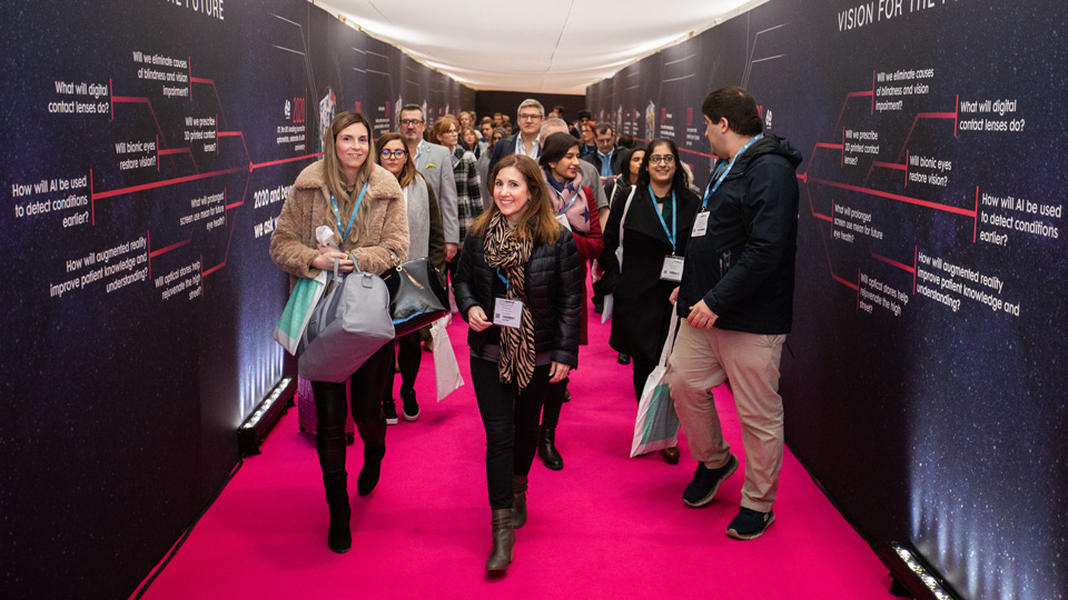 A group of professionals enter 100% Optical through the registration tunnel. The walls are a speckled navy and the floor is a vibrant fuchsia pink