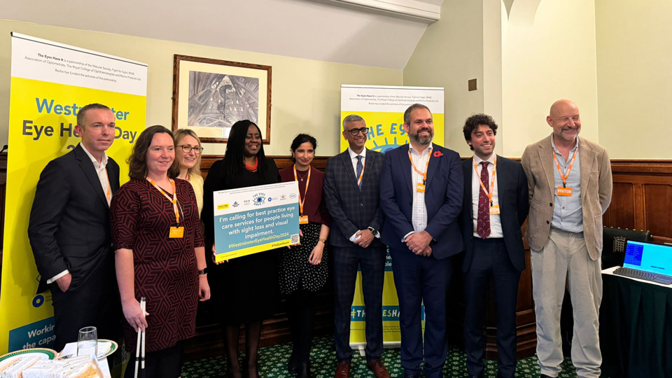 A group of The Eyes Have It members are stood in a line in front of a bright yellow pledge sign 