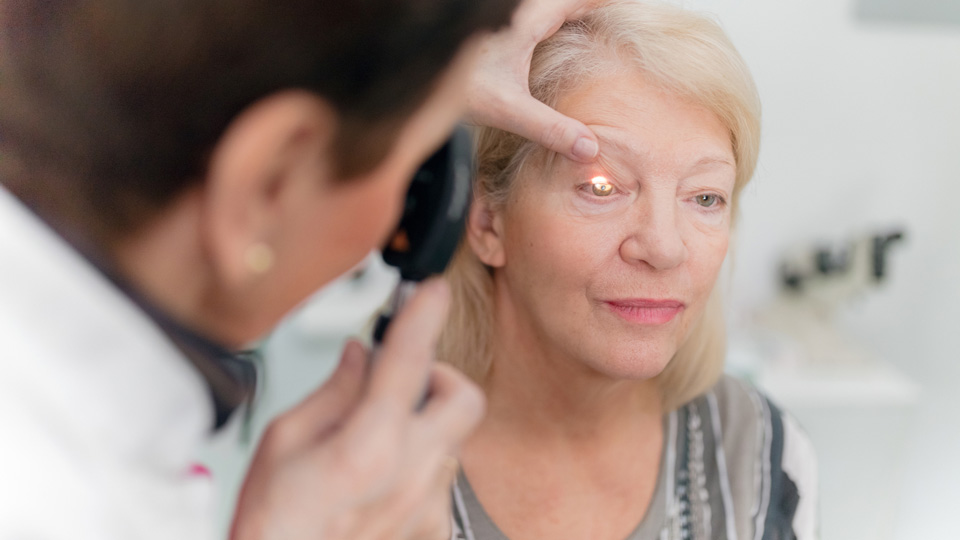 Optometrist looking into the eyes of a white older female patient 