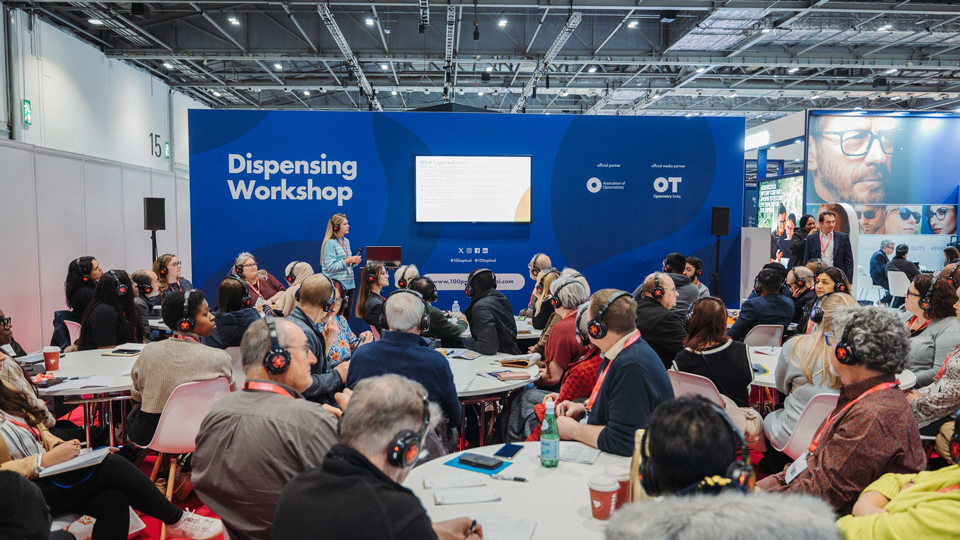 Delegates sit around tables with headphones listening to a session at the Dispensing Workshop stage of 100% Optical 