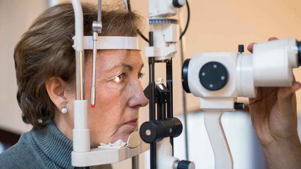 A white woman in her 60s with short brown hair is undergoing an eye exam