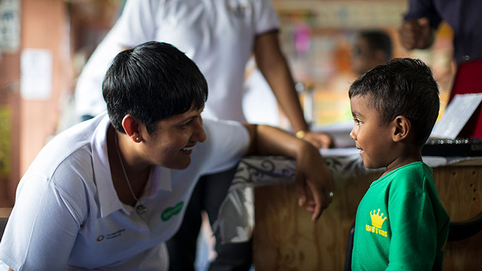 A Specsavers clinicians is crouching down, smiling and chatting with a little boy 