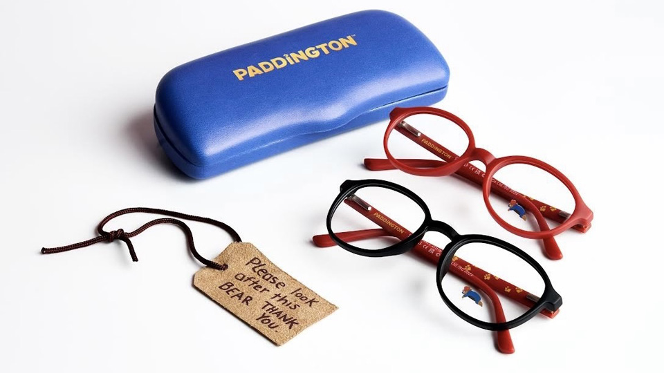 A red frame and black frame with small icons of Paddington bear, with a bright blue glasses case, and a small tag reading ‘Please look after this bear. Thank you.’