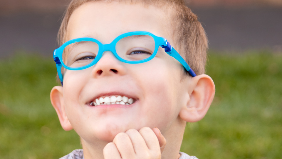 A young boy grins wearing a bright blue pair of spectacles