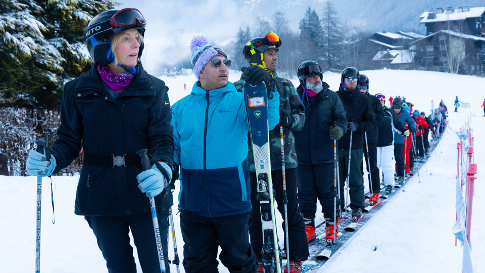 A line of adults on skis are preparing to move off on a ski slope