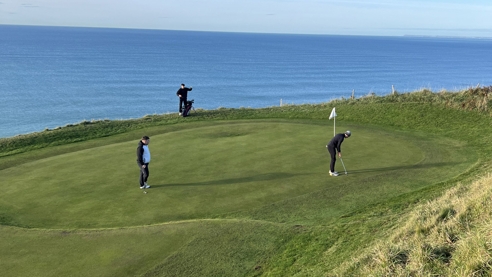A long-distance photograph of a group playing golf by the sea