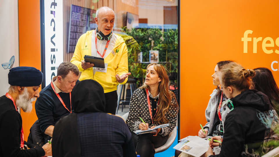 A seminar is in progress at the bright orange CooperVision booth at 100% Optical