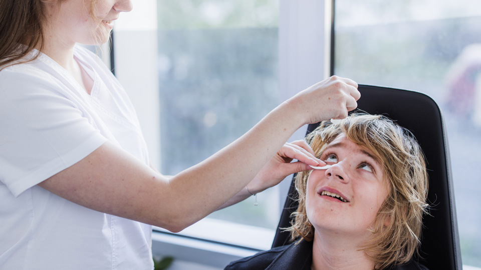 An optometrist instills eye drops in a young patient’s eye