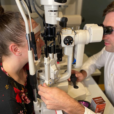 A patient is positioned on the slit lamp, while the optometrist opposite looks through the eyepiece and makes adjustments