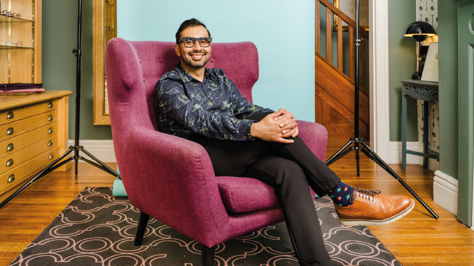Optometrist Deepak Oberai sitting cross legged on a purple chair smiling 